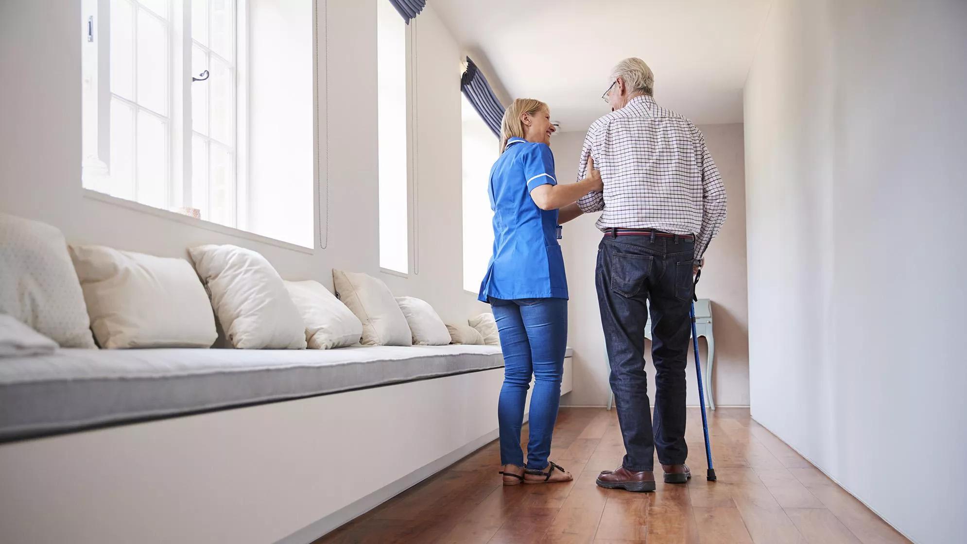 Caregiver helping a senior living resident with a cane walk down a hallway