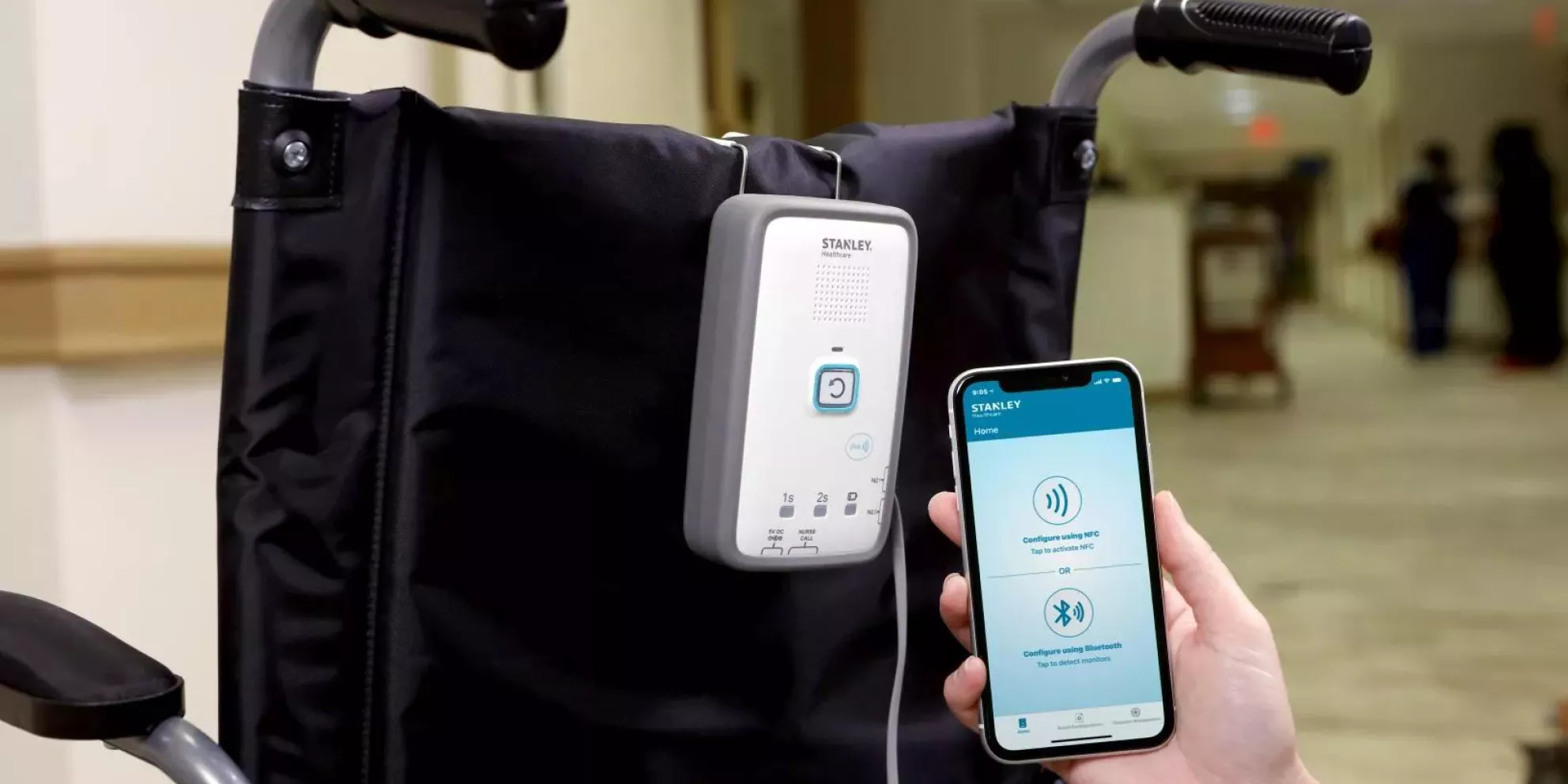 Caregiver holding up an iPhone showing the iOS Mobile Application for the M210 Fall Monitoring System, while the fall monitor is clipped to the back of a wheelchair.