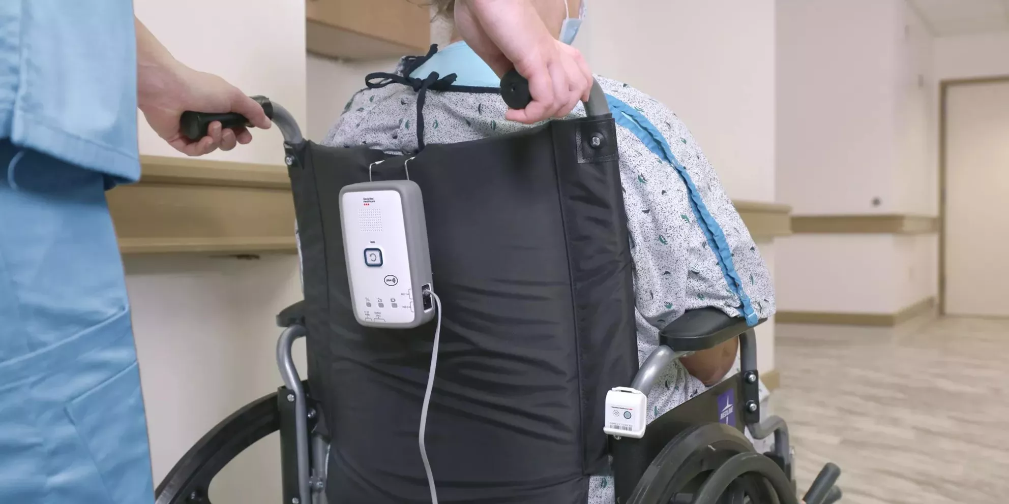 Nurse pushing patient in wheelchair with Securitas Healthcare M210 fall monitor