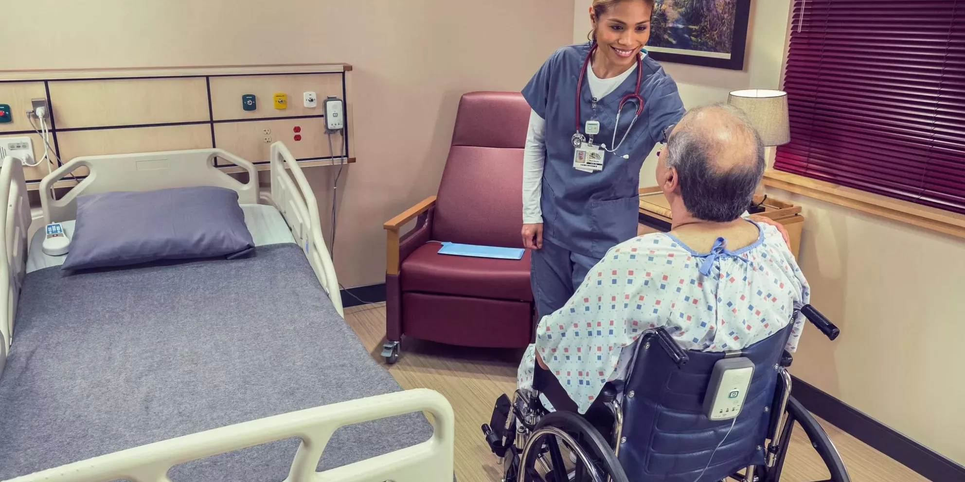 Nurse and patient in wheelchair with Fall Management M210 with hospital bed near by Securitas Healthcare.