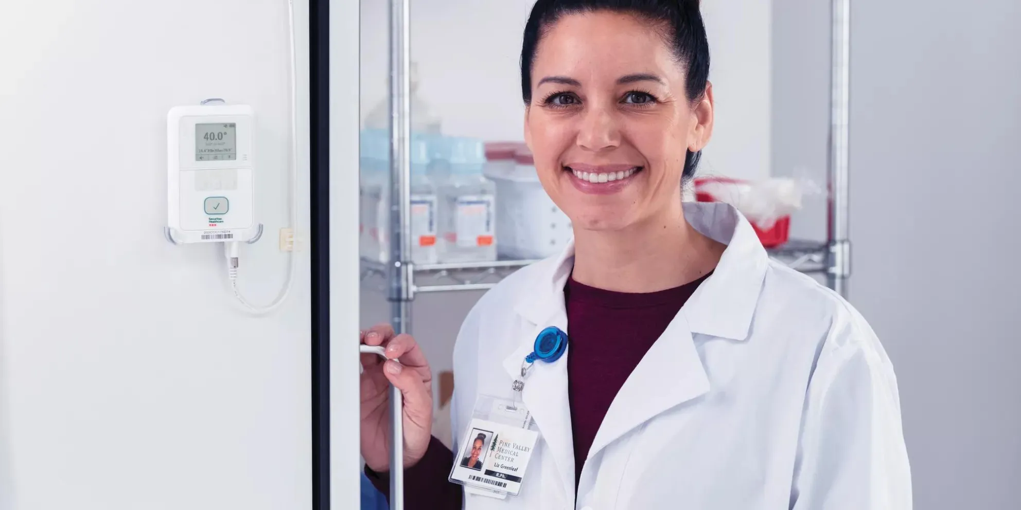 Pharmacist stands by refrigerator with Securitas Healthcare T15e environmental monitoring tag