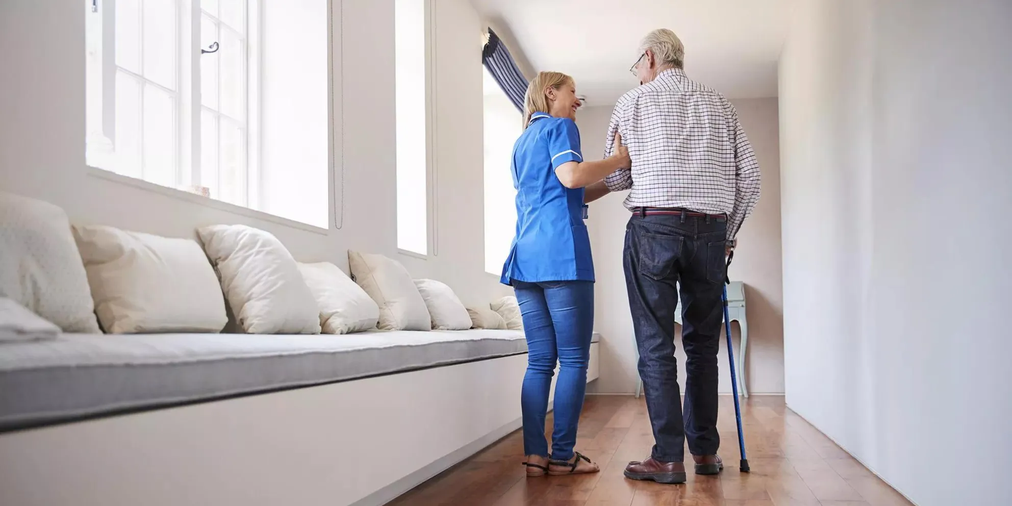 Caregiver helping a senior living resident with a cane walk down a hallway