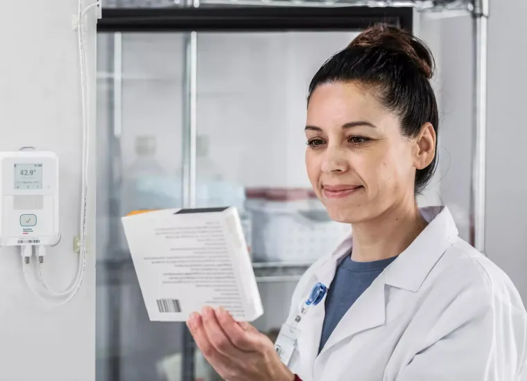 Pharmacist inspecting medicine from refrigerator monitored by Securitas Healthcare T15 environmental monitoring tag.