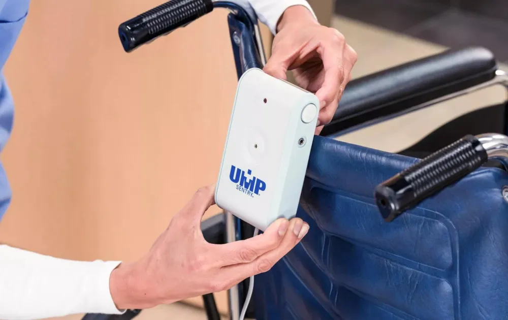 Caregiver attaching UMP Sentry fall monitor to the back of a wheelchair