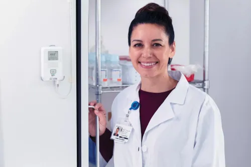 Pharmacist stands by refrigerator with Securitas Healthcare T15e environmental monitoring tag