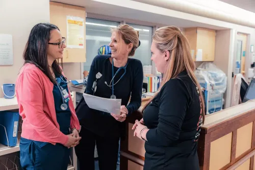 A group of 3 nurses gathered and talking .
