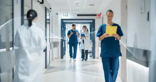 Healthcare Professionals Walking to Their Examination Rooms, Reception Desk, ICU Units in a Modern Bright Hospital Corridor. Female Doctor Showing a Young Male Surgeon Information on a Tablet