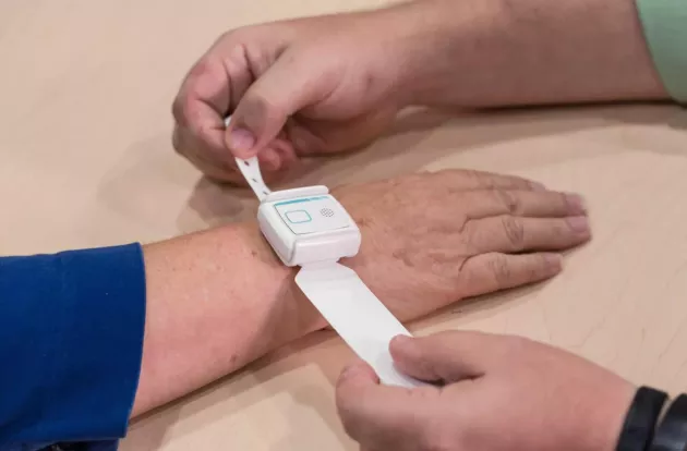 Caregiving fitting the Securitas Healthcare T14 Patient Badge to a patient's wrist.