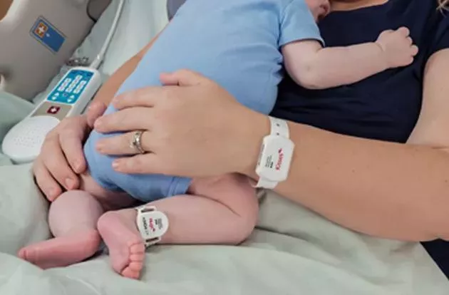 Mom holding baby with Hugs Infant Protection badge while wearing Mother Kisses band on her wrist.