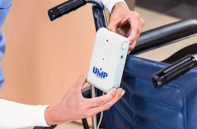 Caregiver attaching UMP Sentry fall monitor to the back of a wheelchair