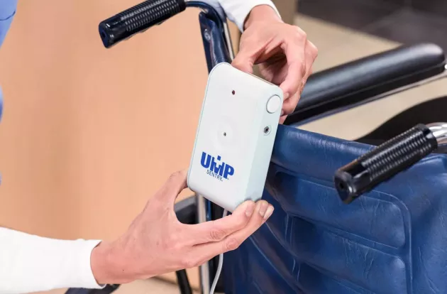 Caregiver attaching UMP Sentry fall monitor to the back of a wheelchair