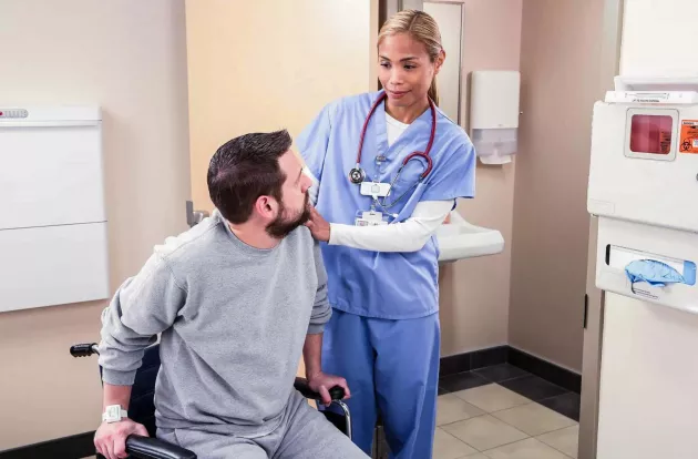 Caregiver helping patient transfer from a wheelchair, while wearing Securitas Healthcare's T3s staff visibility badge.