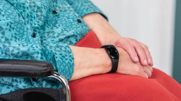Senior community resident seated in wheelchair has her hands folded in lap, wearing a WanderGuard wander management bracelet. Securitas Healthcare.
