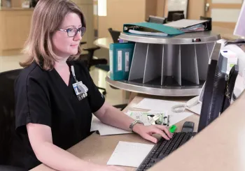 Caregiver on computer behind the nursing station