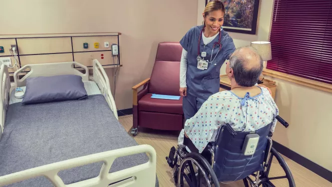 Nurse and patient in wheelchair with Fall Management M210 with hospital bed near by Securitas Healthcare.