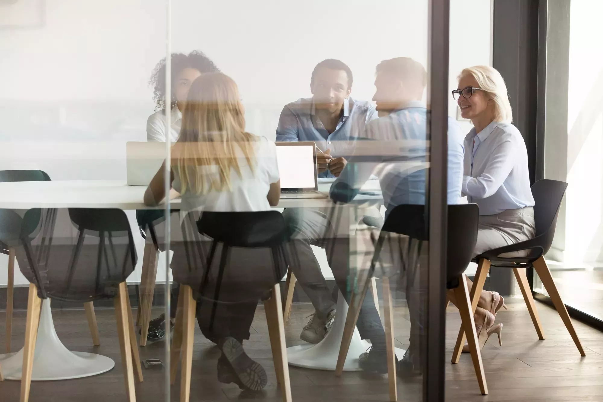 Diverse businesspeople sit at office desk brainstorm together discuss project at meeting, multiethnic employees talk negotiate in conference room share ideas cooperating in boardroom at briefing