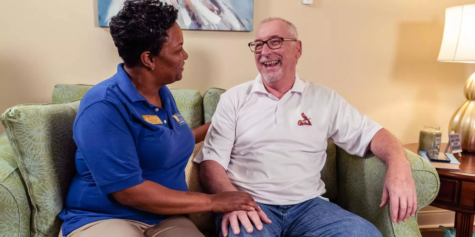 Caregiver assisting and sitting next to a senior living resident on a couch