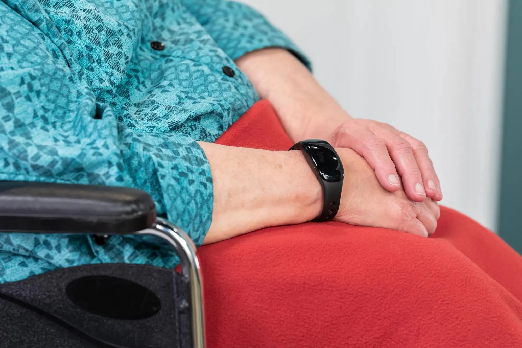 Senior community resident seated in wheelchair has her hands folded in lap, wearing a WanderGuard wander management bracelet. Securitas Healthcare.
