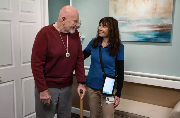 WanderGuard BLUE and Arial nurse call pendant on a senior living resident with caregiver assisting. Securitas Healthcare.