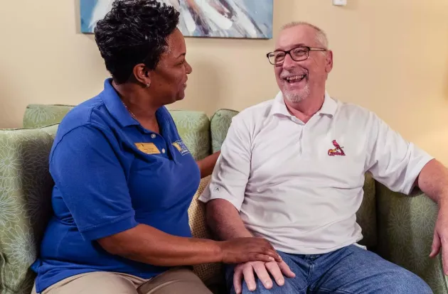 Caregiver assisting and sitting next to a senior living resident on a couch