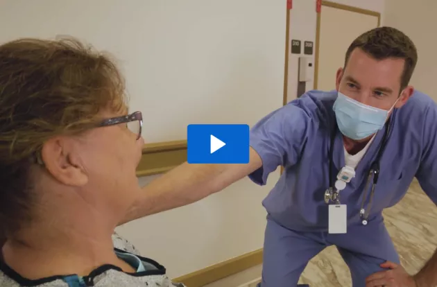 Photo of caregiver dressed in scrubs placing their hand on a patient's shoulder