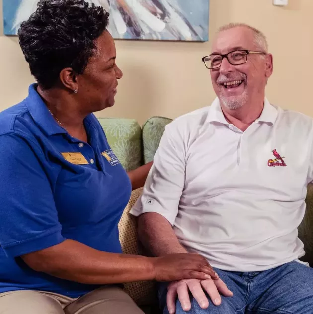 Caregiver assisting and sitting next to a senior living resident on a couch