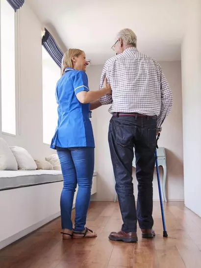 Caregiver helping a senior living resident with a cane walk down a hallway