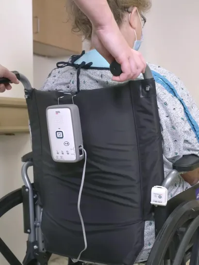 Nurse pushing patient in wheelchair with Securitas Healthcare M210 fall monitor