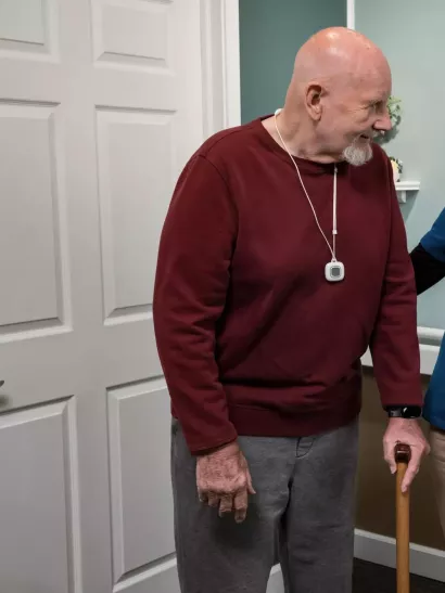 WanderGuard BLUE and Arial nurse call pendant on a senior living resident with caregiver assisting. Securitas Healthcare.