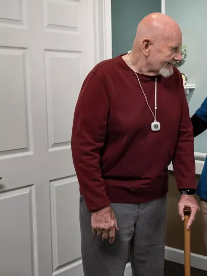 WanderGuard BLUE and Arial nurse call pendant on a senior living resident with caregiver assisting. Securitas Healthcare. 