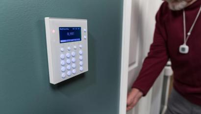 Resident wearing a Securitas Healthcare Arial pendant, entering room near an access point for WanderGaurd Blue. 