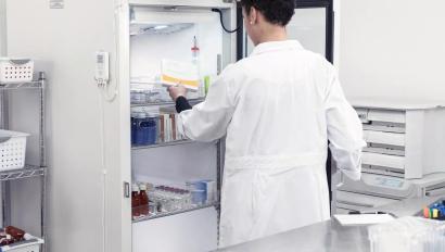 A pharmacist placing temperature-sensitive materials into a medication fridge while the T15e digital data logger monitors temperature.